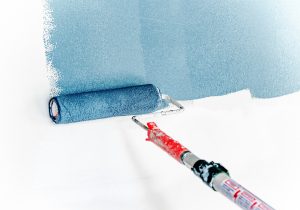 A shot of a paint roller dipped in blue paint running over a white wall.